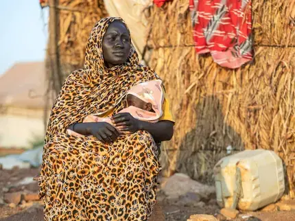 Malka, a displaced mother, carries her 1-year-old daughter Sahar who is suffering severe acute malnutrition outside her house in Elhoury gathering point for internally displaced persons in Gedaref state, November, 2024. Photo: UNICEF/UNI689368/Ahmed Mohamdeen Elfatih.