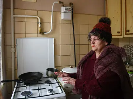 An elderly Ukrainian woman warms herself with a gas stove