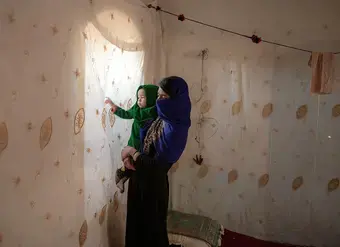 An Afghan mother holds her daughter, staring at the light from behind her obscured window. Photo: UN Women/Sayed Habib Bidell.