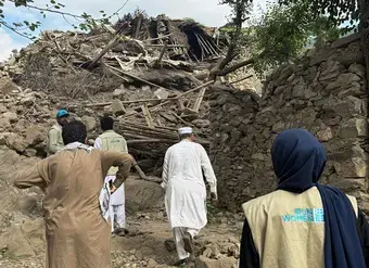 A group of people walk through the crumbled remains of buildings after an earthquake