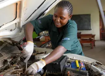 A woman works on a car engine
