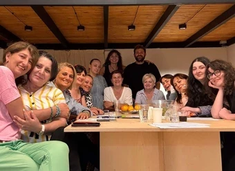 A group of mostly women squeeze together for a big group photo around a table