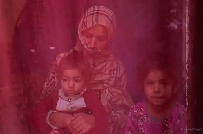 Now unemployed, a woman sits at home with her two daughters. Photo: UN Women/Sayed Habib Bidell.