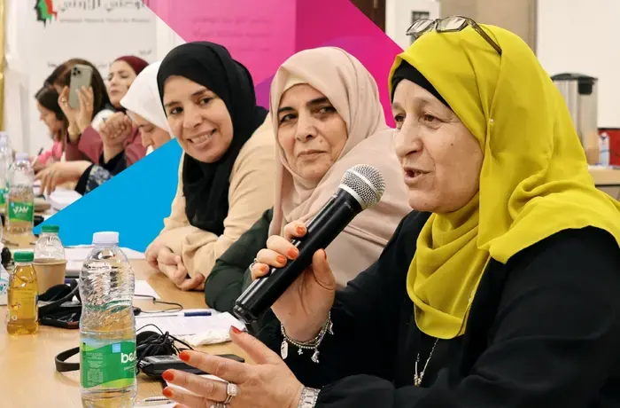 A Jordanian woman with glasses speaks into a microphone as other women listen closely