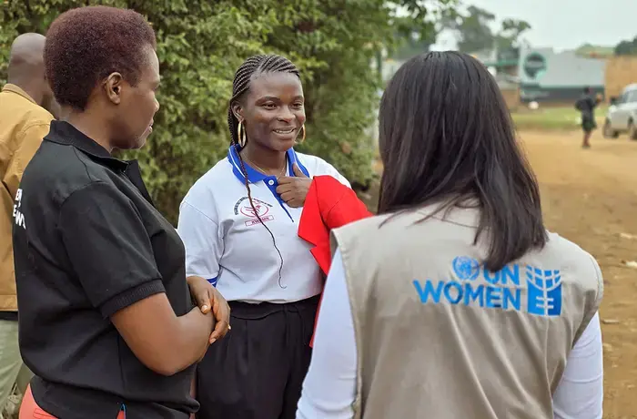 A young woman peacebuilder speaks with two women wearing UN Women vests