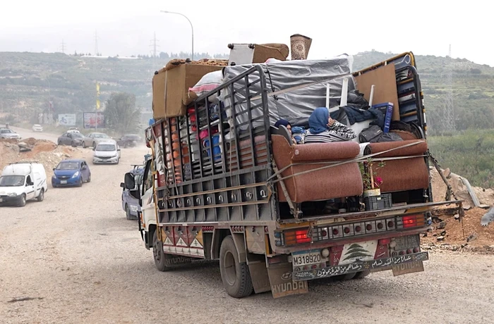 A family sits in the back of a truck, surrounded by their belongings