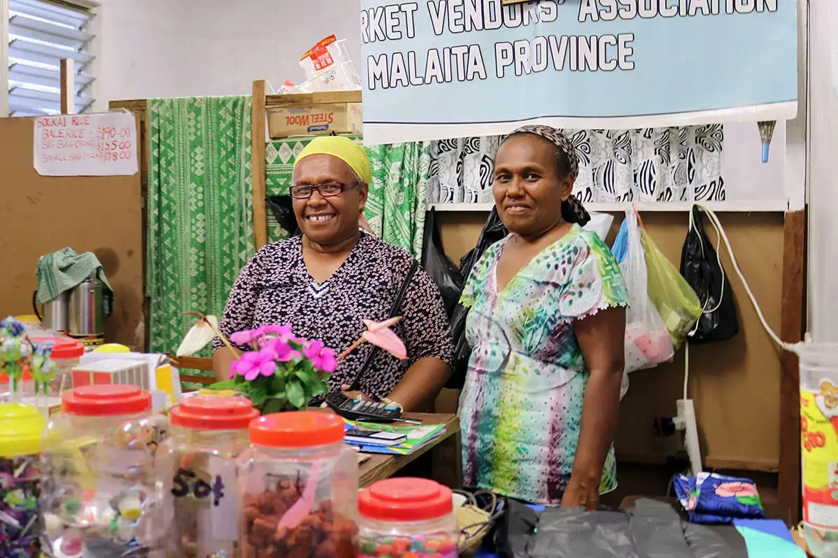 Two women pose behind a market stand