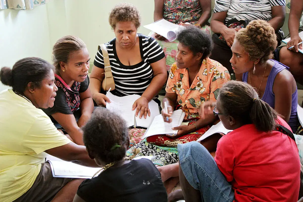 Ten women sit together with workbooks and complete a group exercise with UN Women.