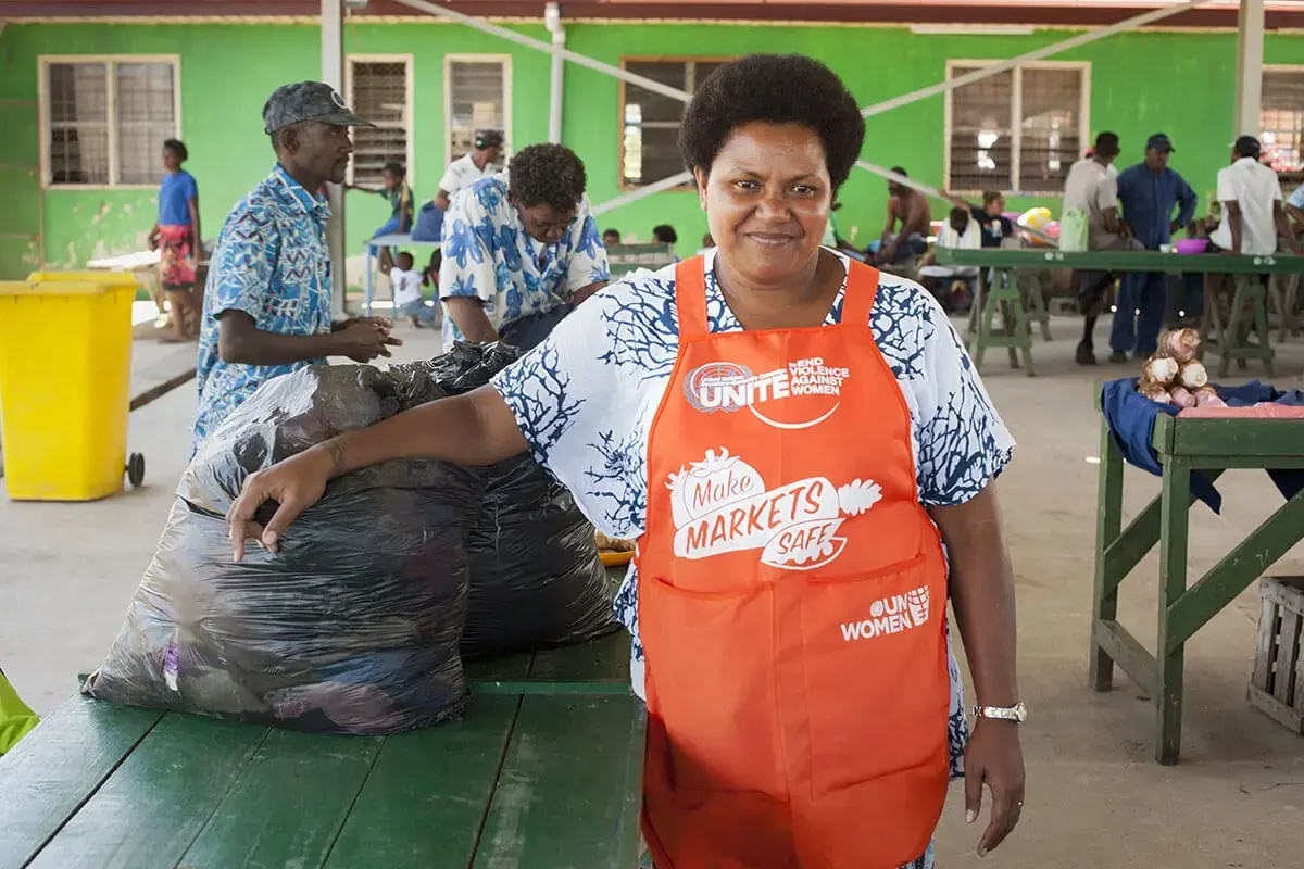 A woman market vendor proudly poses wearing an orange UN Women apron