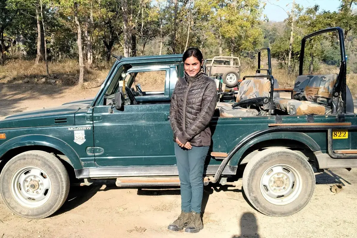 A young woman tour guide stands in front of a Jeep