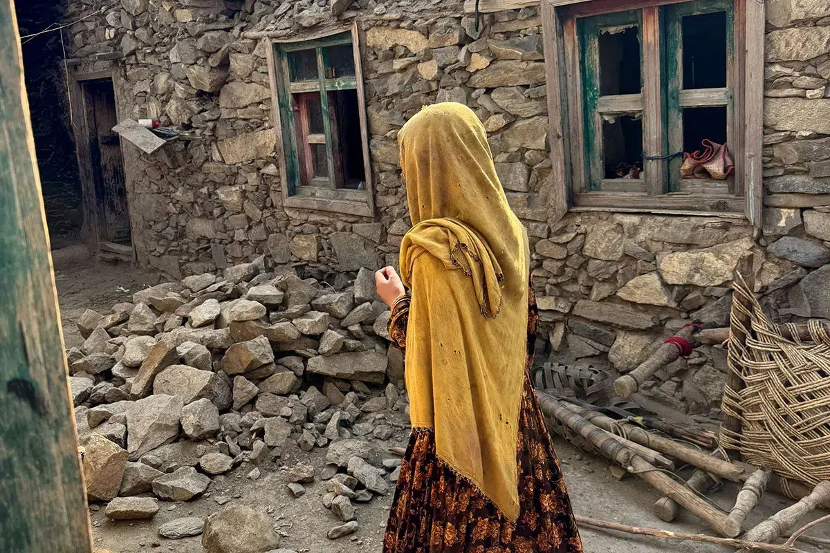 A young woman walks among the stone rubble of a house