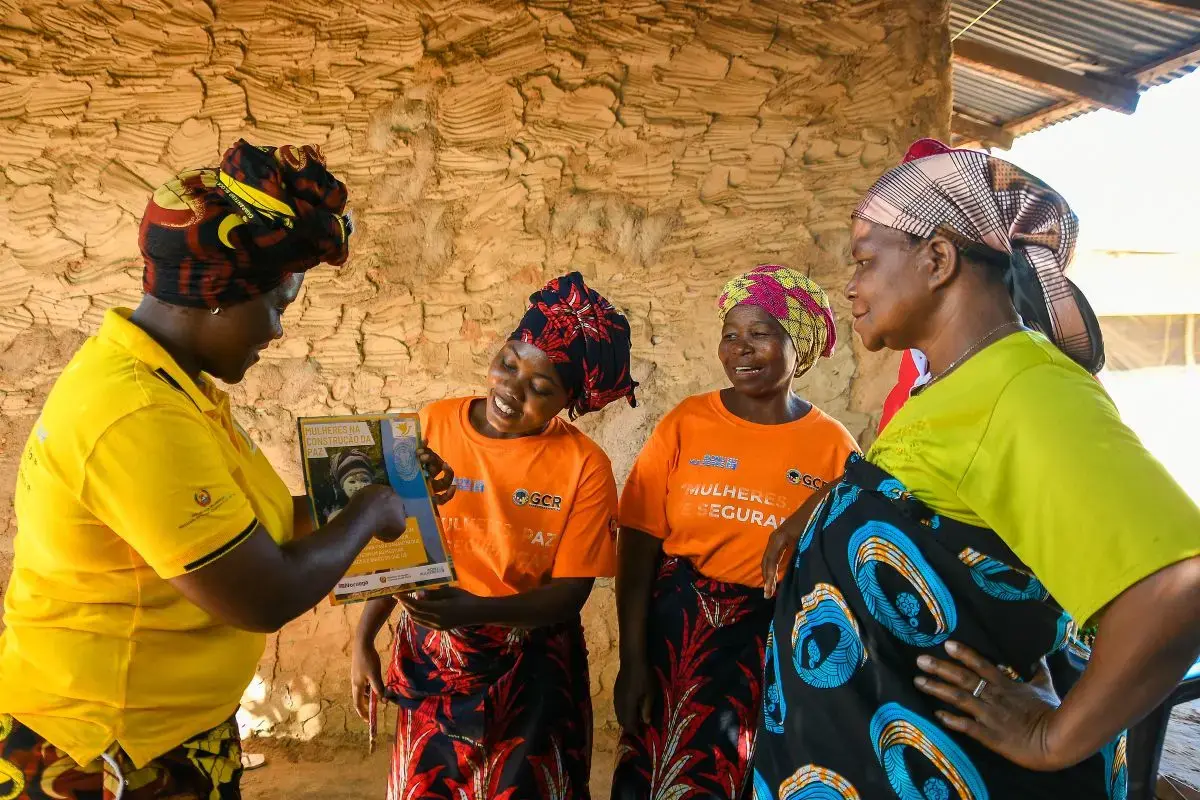 Four women peacebuilders hold up a printed report