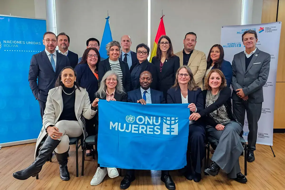 A group of officials pose for a photo in a meeting room, holding an “ONU Mujeres” banner with national and UN flags in the background.