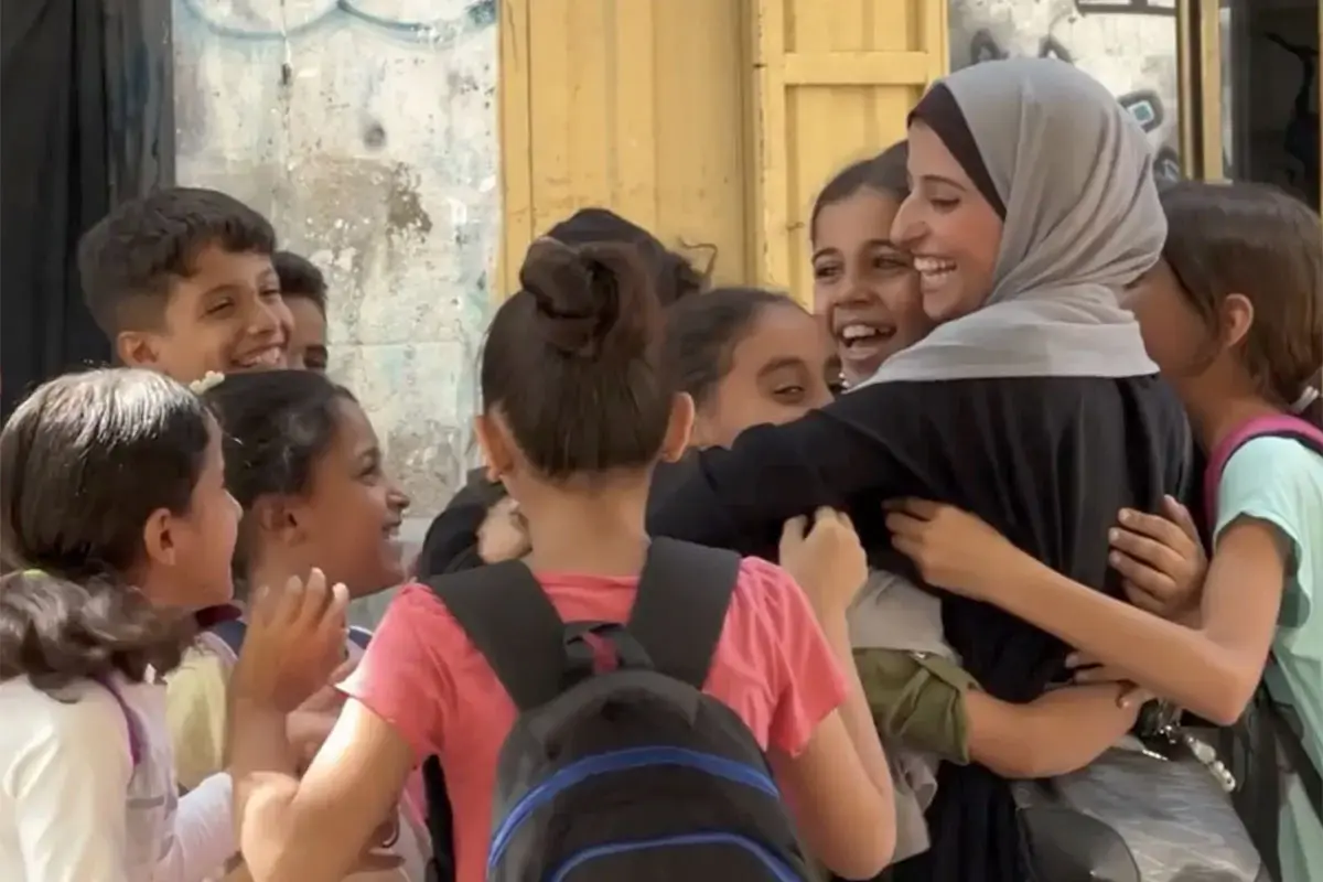 A female teacher smiles and embraces a group of children in Gaza.