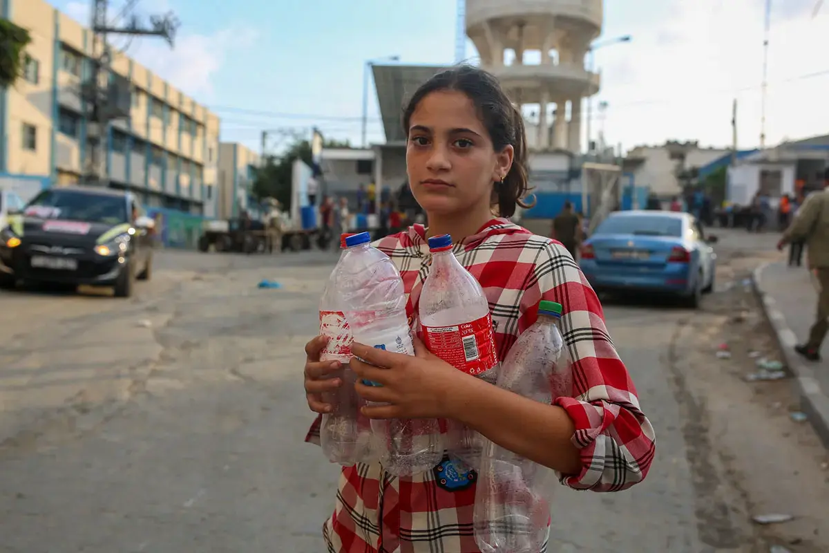 Une jeune fille se tient dans la rue, tenant plusieurs bouteilles en plastique vides.