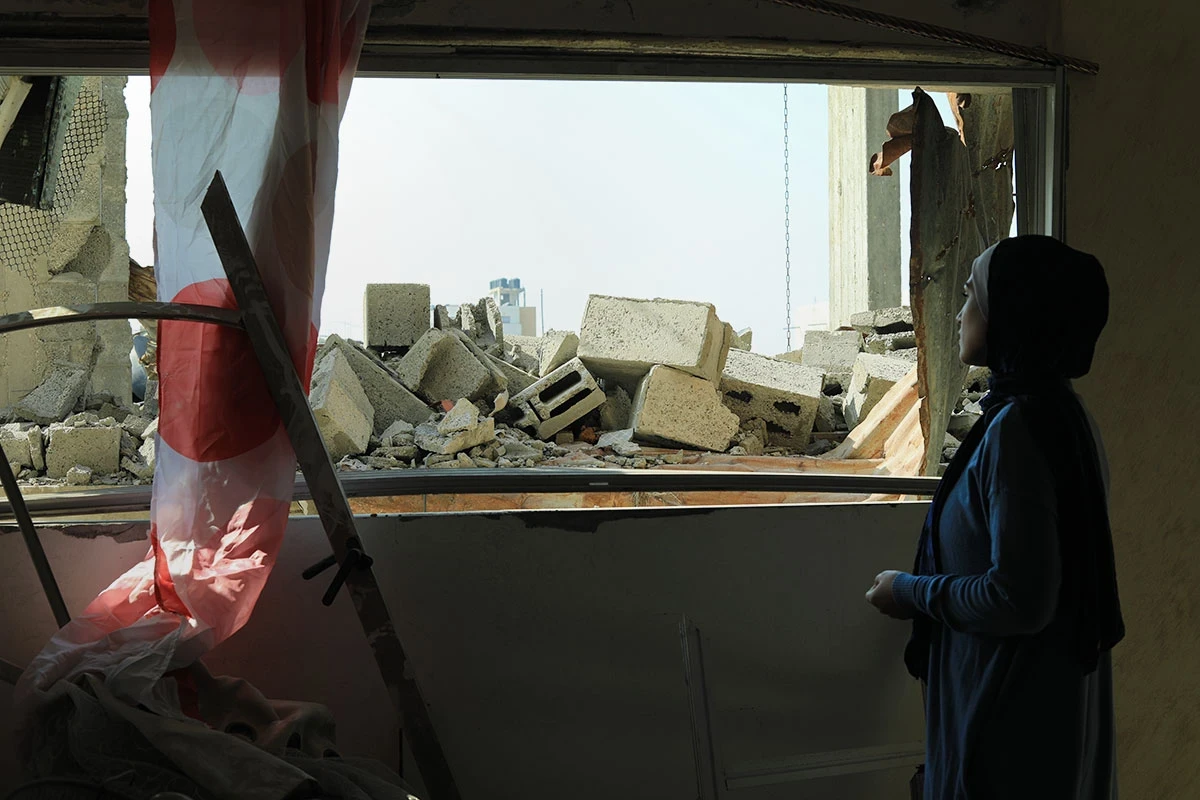 A woman looks out at rubble from inside a ruined building.