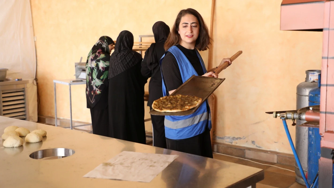 A young woman with a UN Women vest helps local women bake bread with za'atar