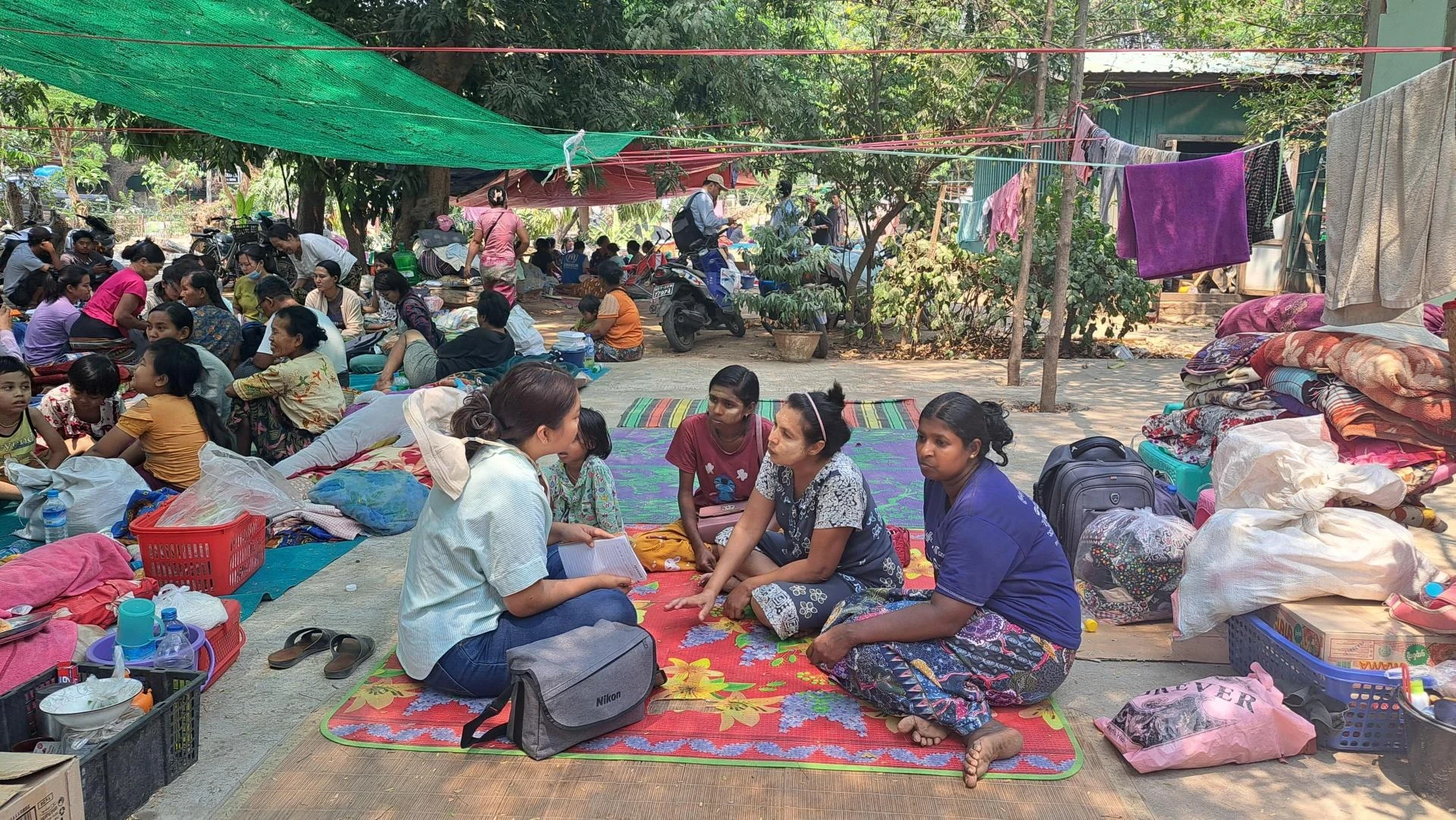 Women sit together on the ground as one woman interviews people about their experiences after a recent earthquake