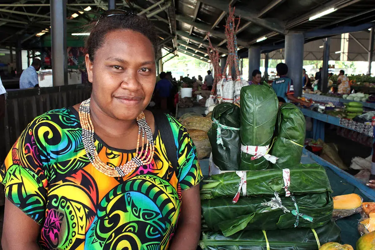 A portrait of a woman in front of produce wrapped in large leaves.