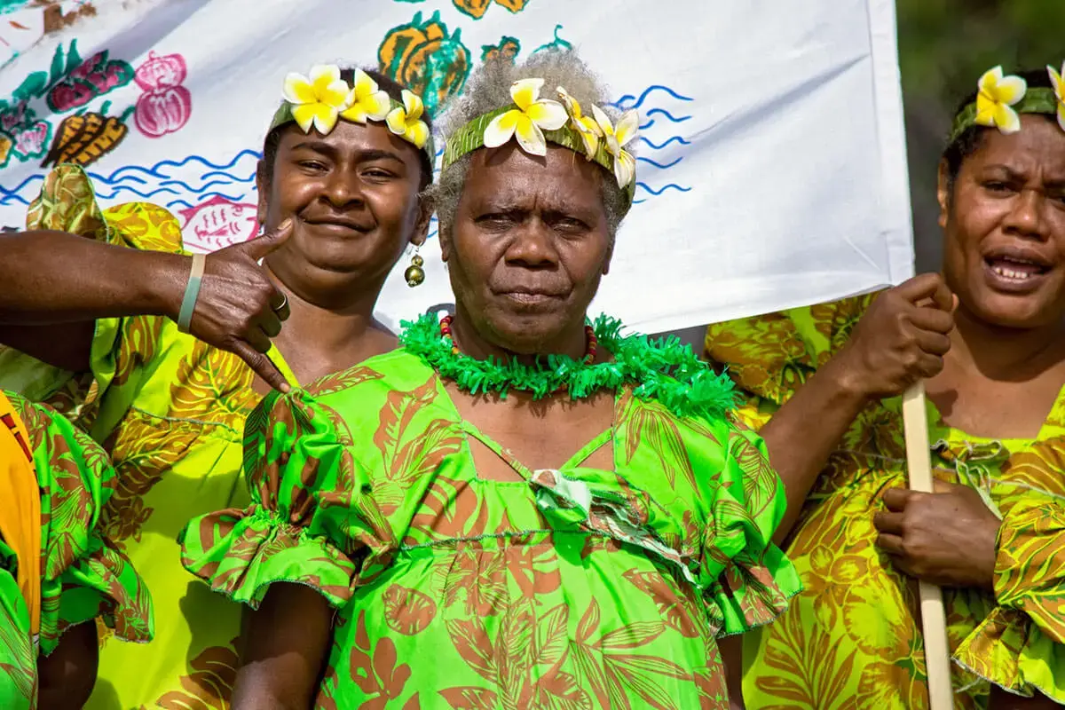 Three women in green traditional dress and flower headdresses.