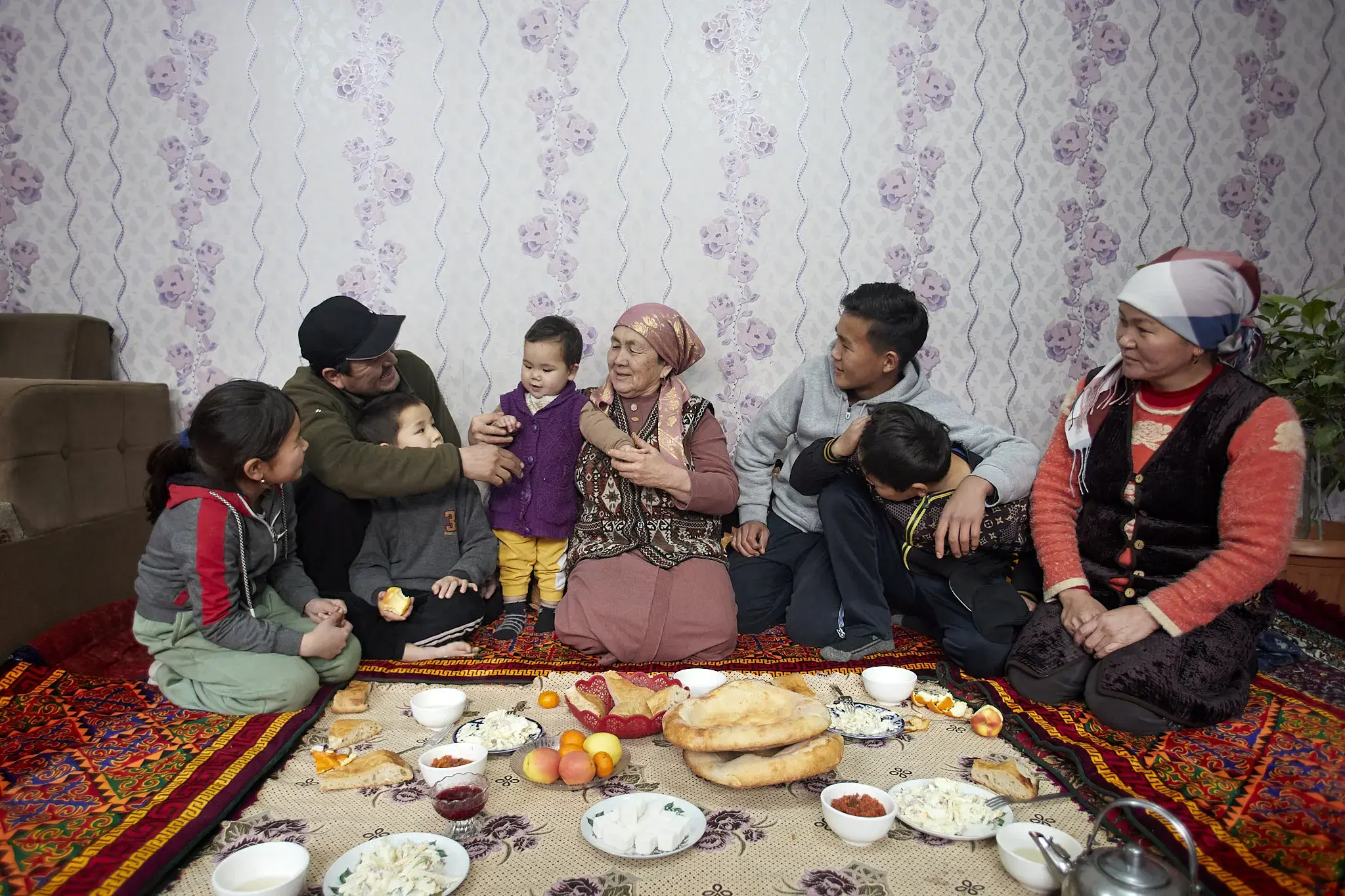 A photo of a happy and affectionate family, seated on the floor next to fresh food they are sharing